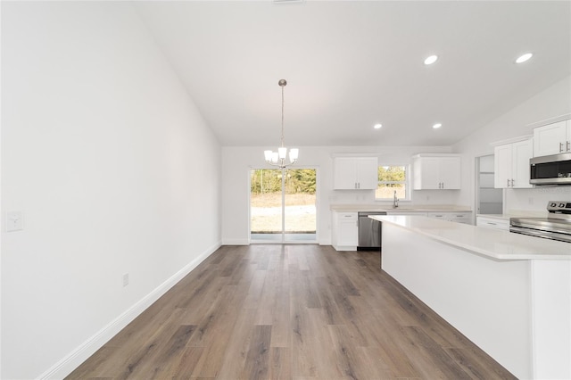 kitchen with appliances with stainless steel finishes, decorative light fixtures, vaulted ceiling, and white cabinets