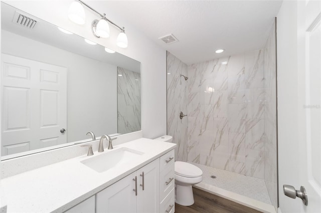 bathroom featuring wood-type flooring, tiled shower, vanity, and toilet