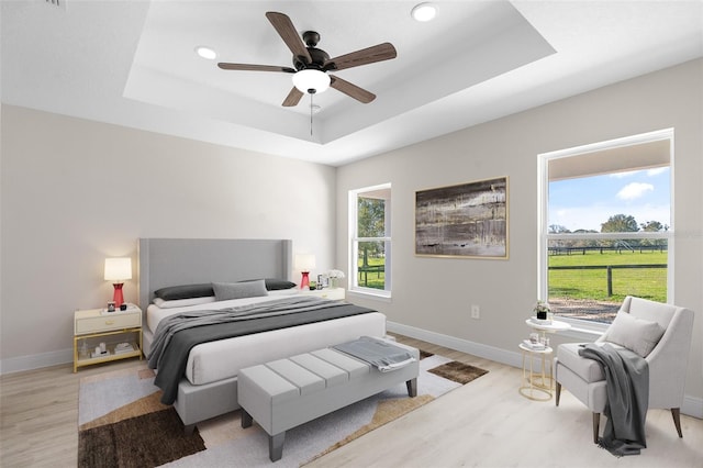 bedroom with light wood-type flooring, ceiling fan, and a raised ceiling