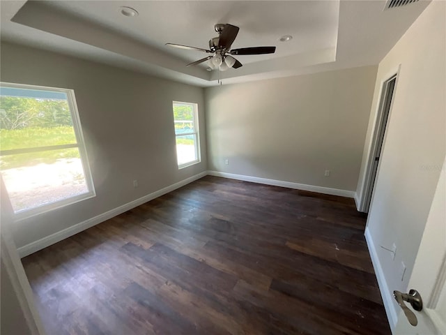 unfurnished room featuring ceiling fan, a tray ceiling, and dark wood-type flooring