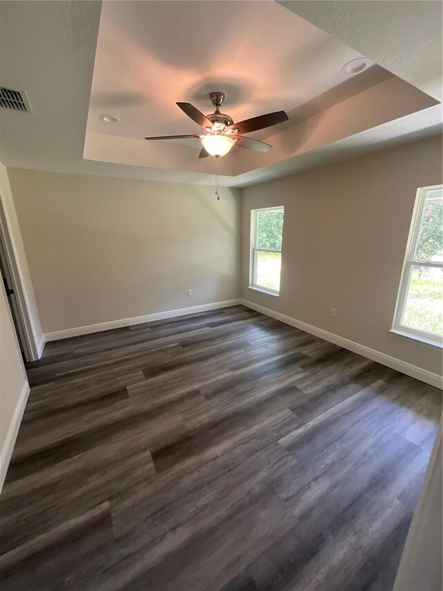 unfurnished room with a tray ceiling, dark hardwood / wood-style floors, and ceiling fan