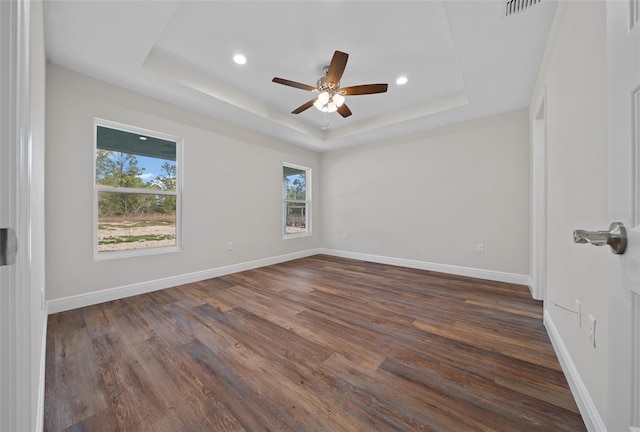 empty room with ceiling fan, dark wood-type flooring, and a raised ceiling