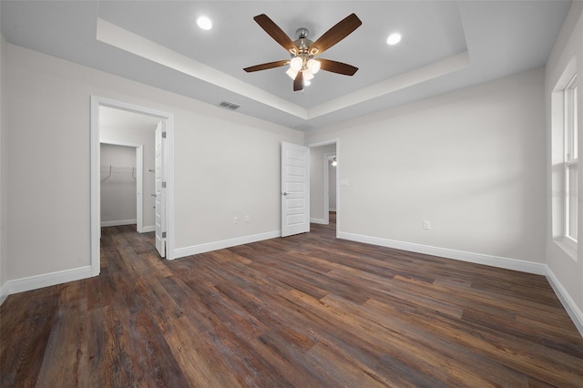 unfurnished bedroom featuring ceiling fan, a walk in closet, a tray ceiling, and dark hardwood / wood-style flooring