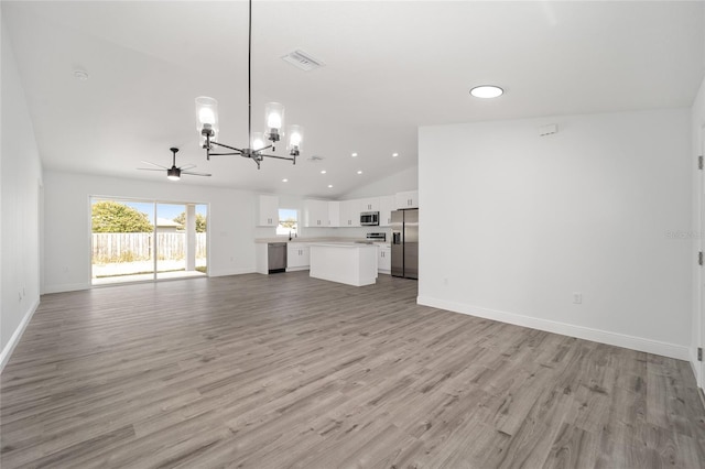 unfurnished living room with ceiling fan with notable chandelier, high vaulted ceiling, and light hardwood / wood-style flooring