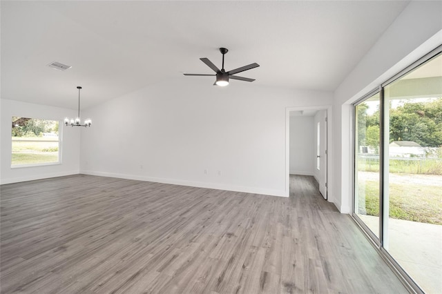 spare room featuring ceiling fan with notable chandelier, light wood-type flooring, and vaulted ceiling