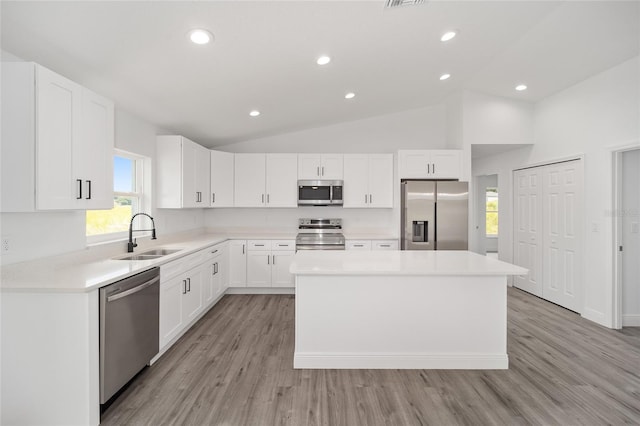 kitchen featuring a center island, sink, vaulted ceiling, appliances with stainless steel finishes, and white cabinetry