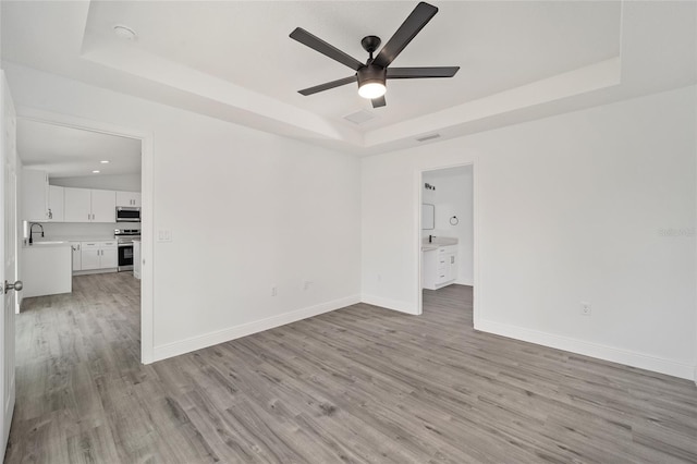 unfurnished room with ceiling fan, light wood-type flooring, sink, and a tray ceiling