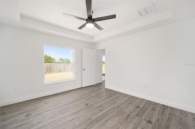 empty room with light hardwood / wood-style flooring, a raised ceiling, and ceiling fan