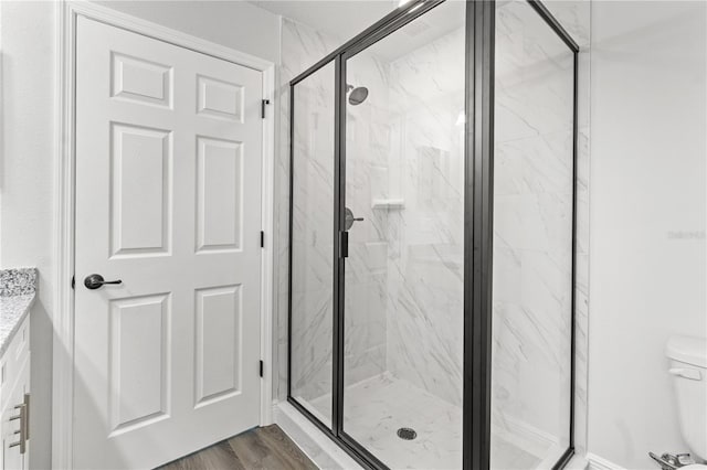 bathroom with toilet, wood finished floors, and a marble finish shower