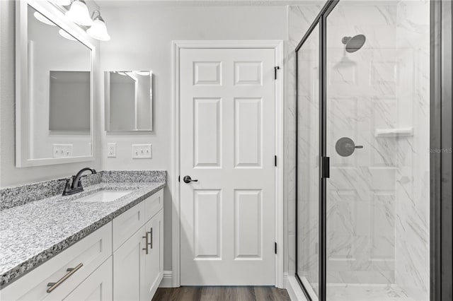 full bath with a marble finish shower, wood finished floors, and vanity