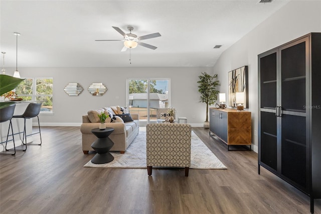 living area featuring visible vents, baseboards, a healthy amount of sunlight, and dark wood-style flooring