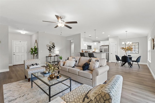 living area featuring ceiling fan with notable chandelier, recessed lighting, baseboards, and light wood-style floors