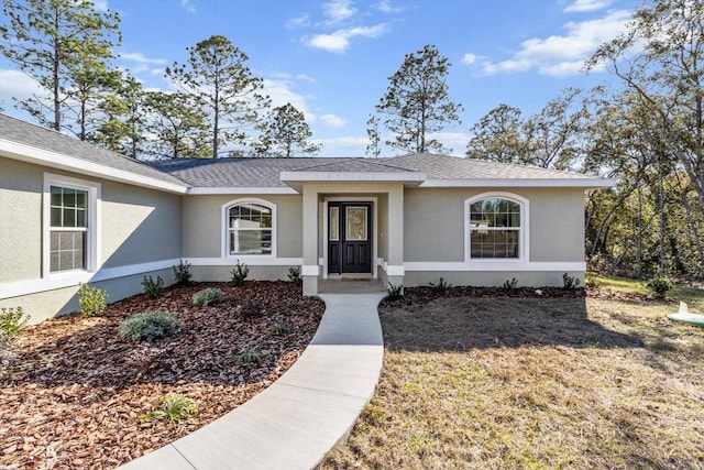 view of front of house featuring a shingled roof, a front yard, and stucco siding