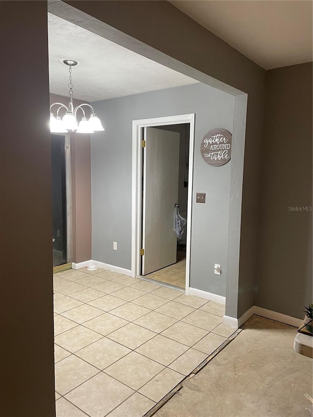 tiled empty room featuring an inviting chandelier