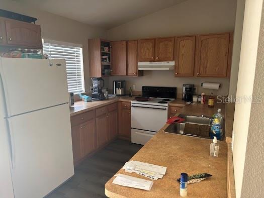 kitchen with lofted ceiling, white appliances, under cabinet range hood, and light countertops