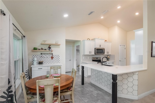 kitchen with kitchen peninsula, vaulted ceiling, stainless steel appliances, and white cabinetry