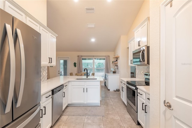 kitchen with lofted ceiling, white cabinets, sink, appliances with stainless steel finishes, and kitchen peninsula