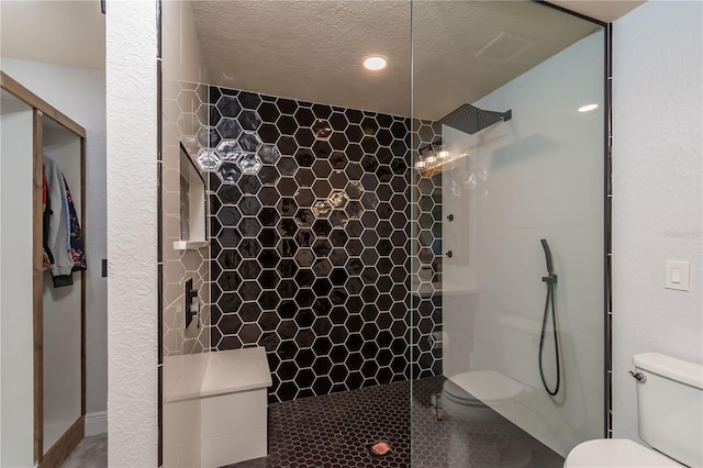 bathroom with toilet, a textured ceiling, and tiled shower