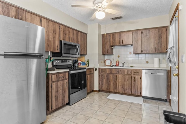 kitchen featuring ceiling fan, decorative backsplash, light tile patterned floors, sink, and stainless steel appliances