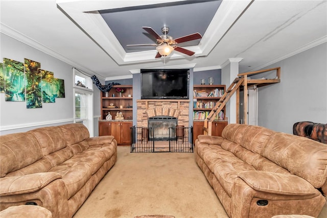 carpeted living room with a tray ceiling, a stone fireplace, ceiling fan, and ornamental molding