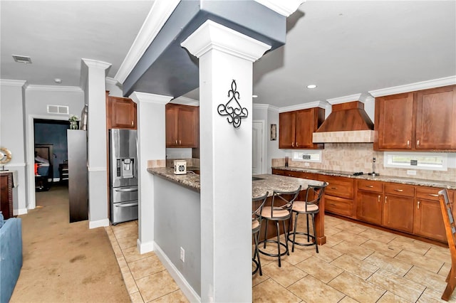 kitchen featuring light stone counters, a breakfast bar, visible vents, stainless steel refrigerator with ice dispenser, and custom exhaust hood