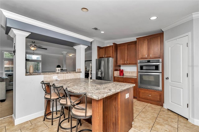 kitchen featuring kitchen peninsula, a kitchen bar, light stone counters, stainless steel appliances, and ceiling fan