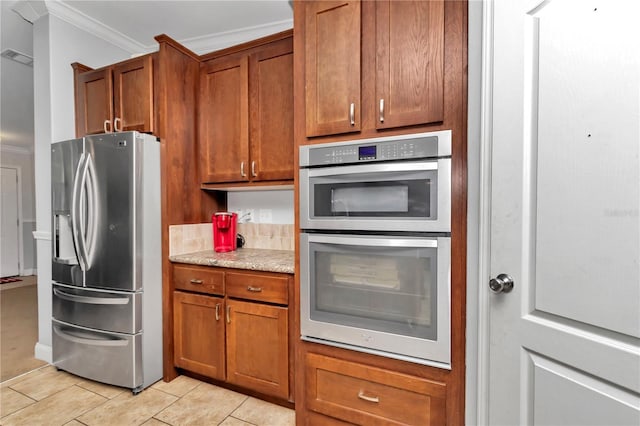 kitchen with light tile patterned floors, light stone counters, brown cabinets, stainless steel appliances, and crown molding