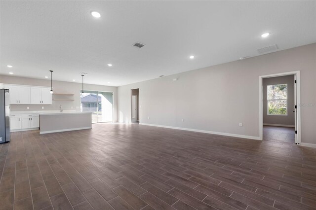 unfurnished living room with plenty of natural light, visible vents, dark wood-style flooring, and recessed lighting