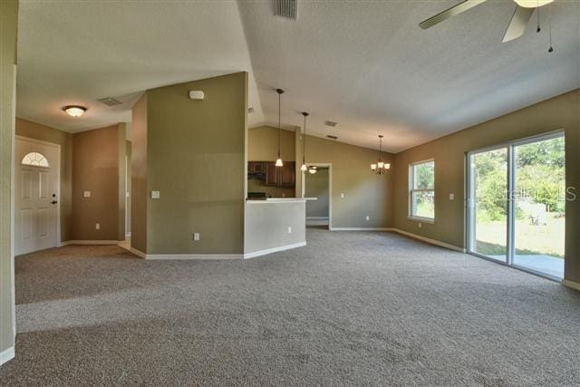 unfurnished living room featuring visible vents, carpet floors, baseboards, lofted ceiling, and ceiling fan with notable chandelier