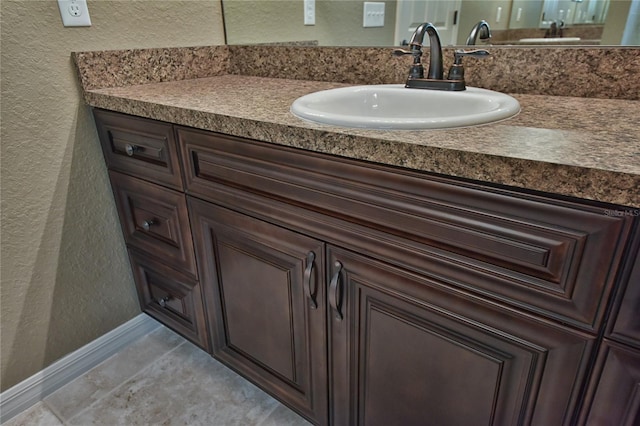 bathroom with vanity, a textured wall, and baseboards