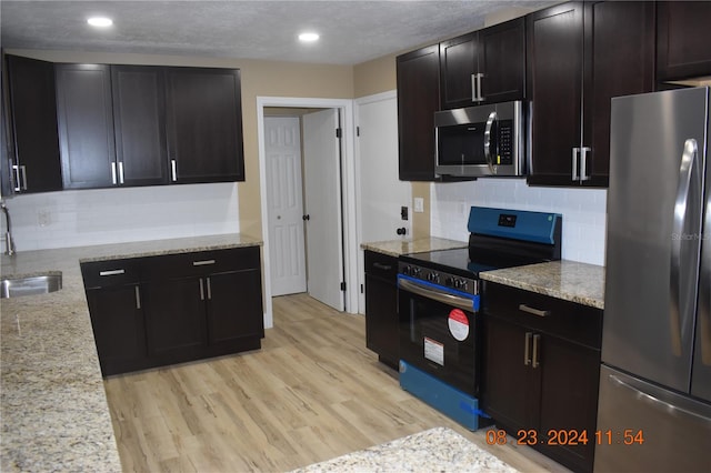 kitchen with light wood-type flooring, backsplash, appliances with stainless steel finishes, light stone counters, and sink