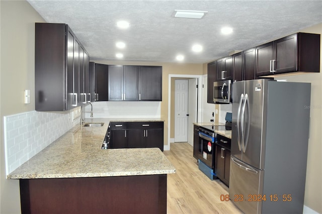 kitchen featuring stainless steel appliances, light hardwood / wood-style floors, decorative backsplash, sink, and a textured ceiling