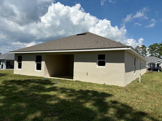 back of house featuring a shingled roof, a lawn, and stucco siding