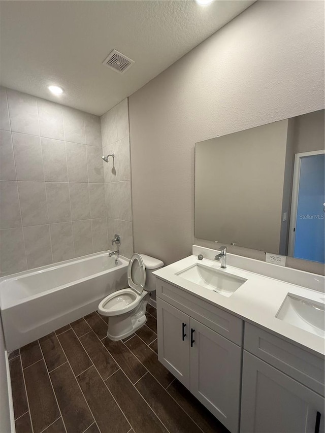 full bathroom with vanity, a textured ceiling, toilet, and tiled shower / bath