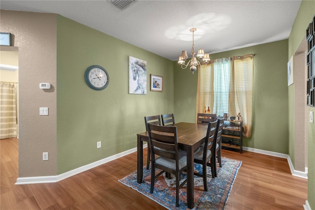 dining room with visible vents, baseboards, wood finished floors, a notable chandelier, and a textured ceiling