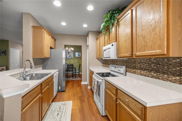 kitchen with white appliances, light wood finished floors, a sink, decorative backsplash, and light countertops