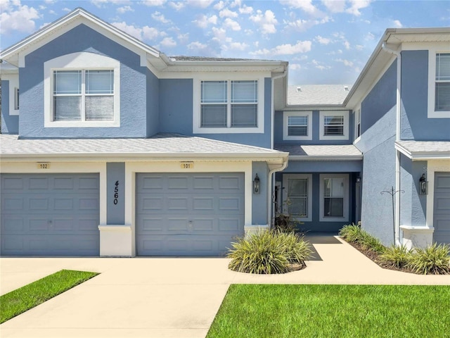 multi unit property featuring a shingled roof, a garage, driveway, and stucco siding