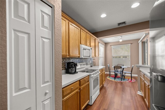 kitchen with white appliances, wood finished floors, ceiling fan, light countertops, and tasteful backsplash