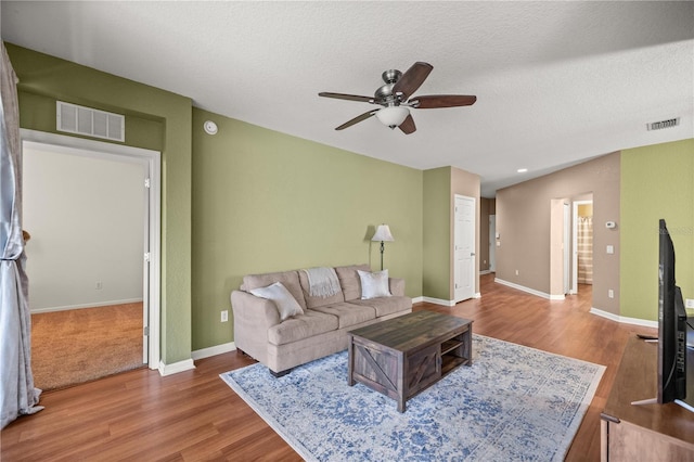 living room with wood finished floors, a ceiling fan, visible vents, and a textured ceiling