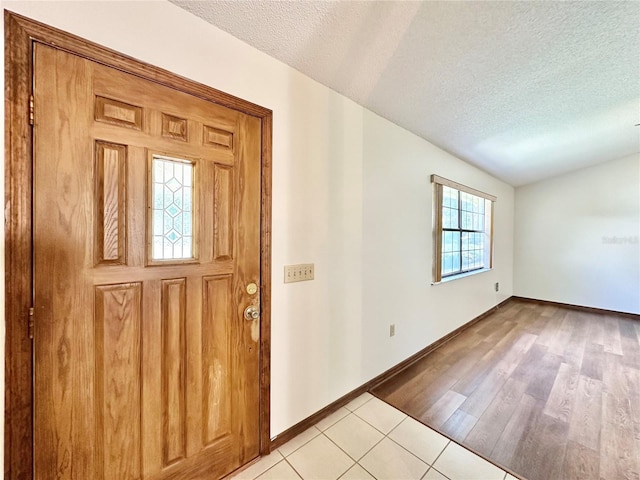 foyer with light wood-type flooring, a textured ceiling, and lofted ceiling