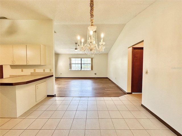 kitchen with ceiling fan with notable chandelier, vaulted ceiling, pendant lighting, and light hardwood / wood-style flooring