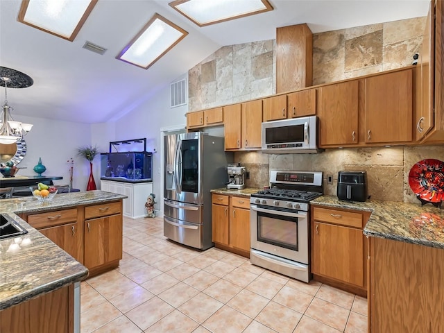 kitchen featuring backsplash, vaulted ceiling, decorative light fixtures, appliances with stainless steel finishes, and light tile patterned flooring