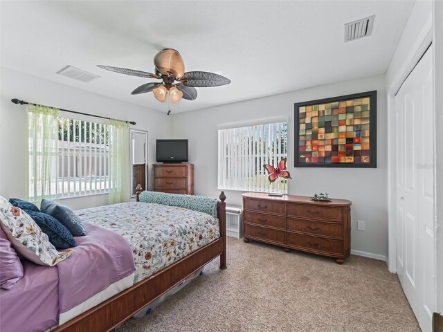 bedroom with multiple windows, light colored carpet, ceiling fan, and a closet