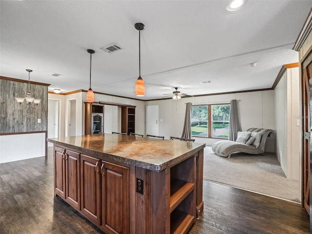 kitchen with pendant lighting, ceiling fan with notable chandelier, crown molding, dark carpet, and a center island