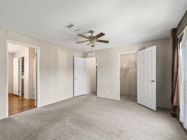 unfurnished bedroom with a spacious closet, carpet, visible vents, and a ceiling fan