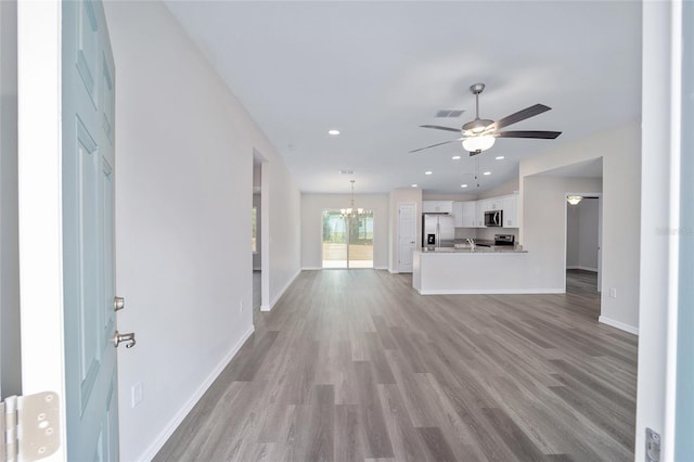 unfurnished living room featuring ceiling fan with notable chandelier and light hardwood / wood-style flooring