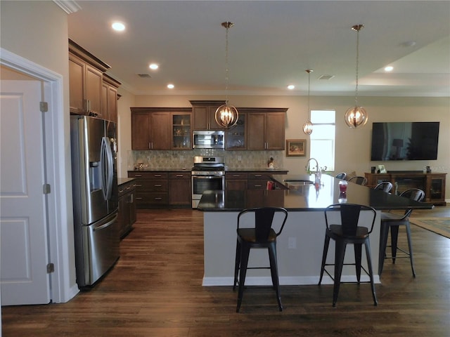 kitchen with pendant lighting, dark wood-type flooring, sink, stainless steel appliances, and a center island with sink