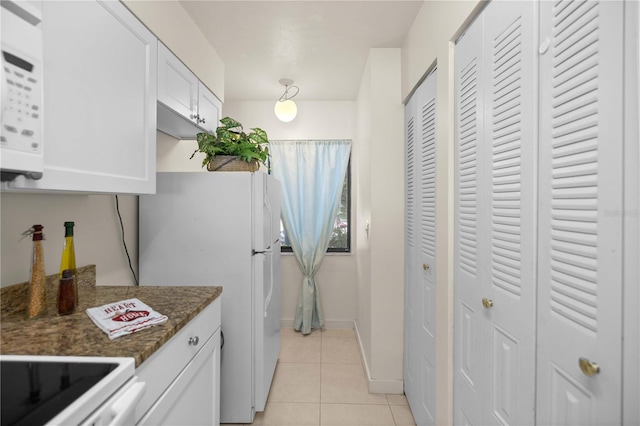 kitchen with white cabinets, stove, light tile patterned flooring, dark stone countertops, and white refrigerator