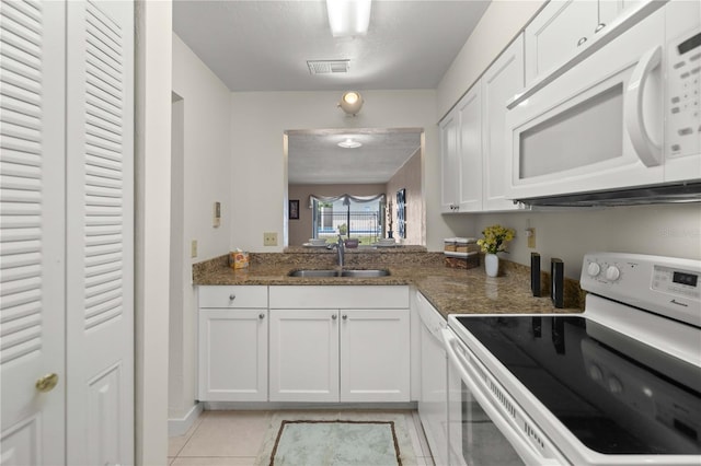 kitchen with sink, dark stone countertops, light tile patterned floors, white appliances, and white cabinetry