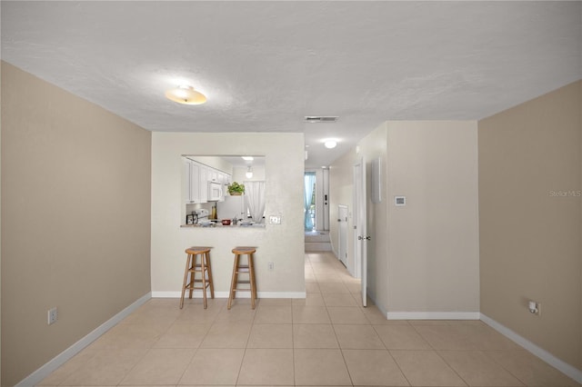 kitchen featuring a kitchen breakfast bar, light tile patterned flooring, and white cabinetry